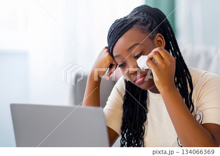 Upset young black lady watching melodrama on laptop and crying, living room interior, copy space. Sad african american woman weeping while watching soap opera, eating popcorn at home Upset young black lady watching melodrama on laptop and crying, living room interior, copy space. Sad african american woman weeping while watching soap opera, eating popcorn at home 134066369
