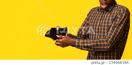 Shocked Black Guy Showing Empty Wallet At Camera, Suffering From Poverty And Absence Of Money, Emotional African Man Having Financial Crisis, Standing Isolated On Yellow Studio Background, Copy Space 134066384