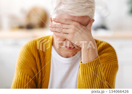 Senior grey-haired woman suffering from migraine, touching her forehead, kitchen interior, closeup. Old lady having headache, experiencing problems with health during climax, climacteric syndrome Senior grey-haired woman suffering from migraine, touching her forehead, kitchen interior, closeup. Old lady having headache, experiencing problems with health during climax, climacteric syndrome 134066426