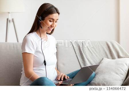 Cheerful Pregnant Woman In Headset Using Laptop At Home, Studying Or Working Online. Smiling Expectant Mother Watching Webinar Or Having Training In Internet, Enjoying Distance Learning And Remote Job 134066472