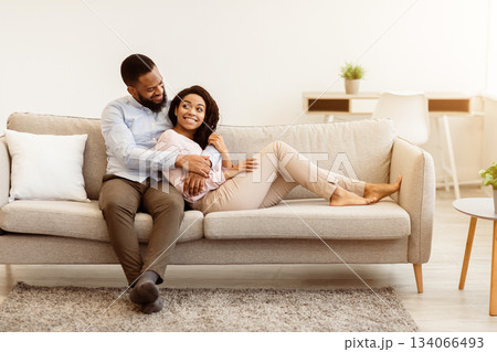 Happy Loving Family. Beautiful african american couple spending weekend together, resting on the couch indoors at home in living room, relaxing and enjoying the company of each other, hugging Happy Loving Family. Beautiful african american couple spending weekend together, resting on the couch indoors at home in living room, relaxing and enjoying the company of each other, hugging 134066493