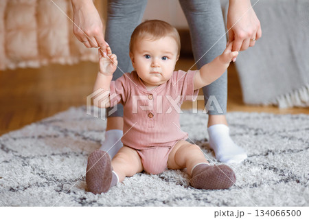 Adorable little kid holding mother hands, sitting on floor, ready for making first steps, copy space. Beautiful blonde baby sitting on carpet at home, holding mummy fingers, looking at camera, closeup Adorable little kid holding mother hands, sitting on floor, ready for making first steps, copy space. Beautiful blonde baby sitting on carpet at home, holding mummy fingers, looking at camera, closeup 134066500