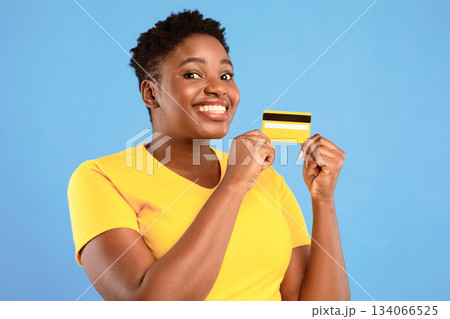 Oversized African Woman Holding Yellow Credit Card Showing It To Camera Advertising Bank Posing Over Blue Studio Background. Banking, Money And Finance, Financial Advertisement Concept Oversized African Woman Holding Yellow Credit Card Showing It To Camera Advertising Bank Posing Over Blue Studio Background. Banking, Money And Finance, Financial Advertisement Concept 134066525