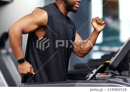 Jogging workout. Joyful black man in modern wireless headphones running on treadmill at gym, looking at free space. Motivated african american guy in black sportswear spending time at gym, jogging 134066526