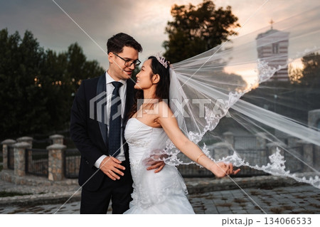Interracial wedding couple embracing at sunset Interracial wedding couple embracing at sunset 134066533