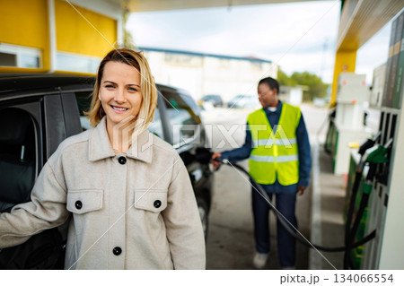 Woman smiling while gas station attendant refueling car Woman smiling while gas station attendant refueling car 134066554