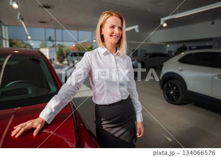 Saleswoman smiling standing beside car in dealership showroom 134066576