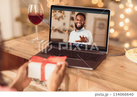 Long Distance Relationship. African american couple having online virtual date, man reaching hand to webcam in videochat with videoconferencing app window, woman showing him present box 134066640