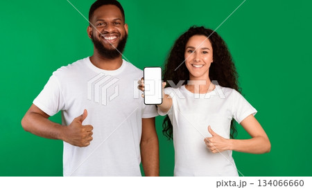 We Like This App. Diverse Couple Showing Smartphone Empty Screen Gesturing Thumbs-Up Approving Mobile Application Standing Over Green Studio Background. Panorama, Mockup 134066660