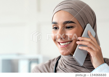 Closeup portrait of cheerful female doctor muslim woman talking on mobile phone and looking at copy space. Smiling young lady in hijab having conversation with patient on smartphone Closeup portrait of cheerful female doctor muslim woman talking on mobile phone and looking at copy space. Smiling young lady in hijab having conversation with patient on smartphone 134066680