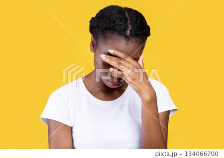 Female Depression. Depressed African American Woman Covering Face With Hand Having Problems And Suffering From Unhappiness Standing Over Yellow Studio Background. Sadness And Frustration Concept 134066700