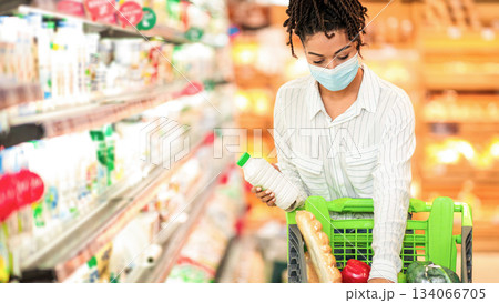 Supermarket Shopping Concept. African American Woman Buying Food Grocery Standing With Pushcart Near Store Shelf Indoors, Wearing Face Mask. Consumerism, Female Customer In Market Shop. Free Space 134066705