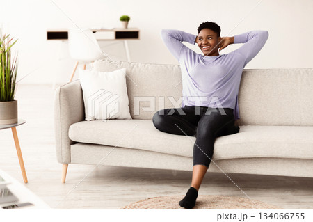 Smiling curvy young black woman with hands behind head relaxing on cozy sofa at home, daydreaming and looking away, satisfied serene girl leaning back, stretching on comfortable couch in living room Smiling curvy young black woman with hands behind head relaxing on cozy sofa at home, daydreaming and looking away, satisfied serene girl leaning back, stretching on comfortable couch in living room 134066755