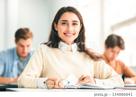 School's in Session. Portrait of cheerful happy female student sitting at table in academic auditorium, posing and looking at camera. Higher educational institutions, learning with pleasure concept 134066841