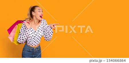Omg, Shopping Offer Concept. Portrait Of Emotional Female Customer Pointing Finger Aside At Copy Space Holding Shopper Bags Isolated Over Pastel Orange Background At Studio, Banner, Panorama Omg, Shopping Offer Concept. Portrait Of Emotional Female Customer Pointing Finger Aside At Copy Space Holding Shopper Bags Isolated Over Pastel Orange Background At Studio, Banner, Panorama 134066864