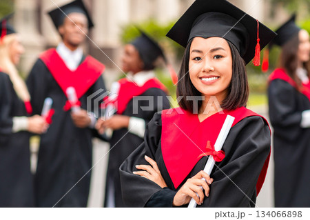 Happy young asian lady student having graduation party, wearing graduation costume and holding diploma, pretty female graduate proudly posing at university campus, blurred background Happy young asian lady student having graduation party, wearing graduation costume and holding diploma, pretty female graduate proudly posing at university campus, blurred background 134066898