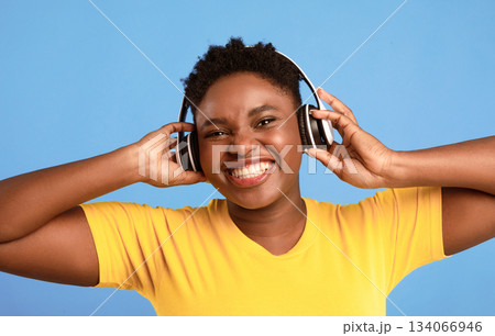 Positive Oversized Black Woman Wearing Wireless Headphones Listening To Music Smiling To Camera Posing Over Blue Studio Background. Great Playlist, Electronics, Music Lover Concept 134066946
