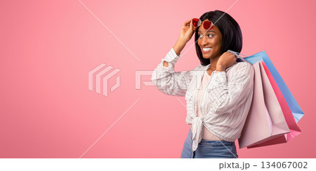 Beautiful black woman with shopping bags looking at empty space for your ad on pink studio background. Pretty female shopper having special offer, promoting big sale, banner design Beautiful black woman with shopping bags looking at empty space for your ad on pink studio background. Pretty female shopper having special offer, promoting big sale, banner design 134067002