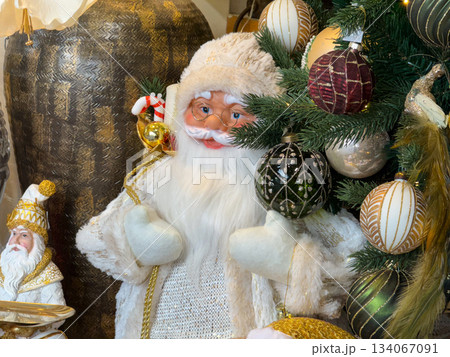 Elegant white Santa figure beside decorated Christmas tree with golden ornaments. Festive luxury, warm winter celebration, nostalgia and traditional holiday joy Elegant white Santa figure beside decorated Christmas tree with golden ornaments. Festive luxury, warm winter celebration, nostalgia and traditional holiday joy 134067091