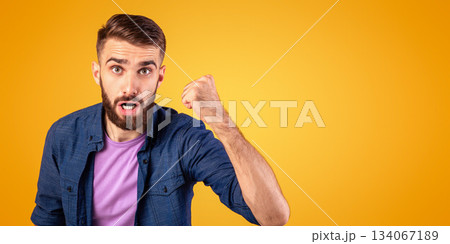 Portrait of young angry guy shaking clenched fist at camera and shouting, showing his protest over orange studio background. Furious millennial man threatening someone, expressing negativity 134067189