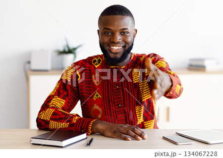 Handsome Black Man In Traditional African Costume Giving Hand For Handshake While Sitting At Desk In Office, Friendly HR Manager Offering Partnership And Job Opportunities, Free Space Handsome Black Man In Traditional African Costume Giving Hand For Handshake While Sitting At Desk In Office, Friendly HR Manager Offering Partnership And Job Opportunities, Free Space 134067228