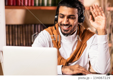 Young Indian Teacher At Laptop Computer Waving Hello To Distant Student Having Online Lecture Webinar Via Video Call Teaching Remotely Sitting At Home. Modern Tutoring, Education And E-Teaching 134067229