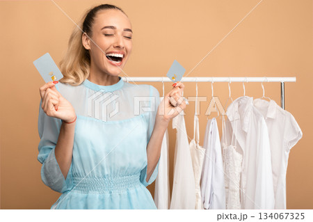 Time For Shopping Concept. Portrait of excited young woman holding and showing two debit credit cards, standing in wardrobe near clothing rail and screaming yes with joy, happy about purchases 134067325