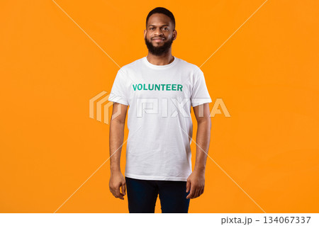 African American Volunteer Man Standing Posing Wearing Uniform T-Shirt, Smiling To Camera Posing Over Yellow Studio Background. Shot Of Activist Advertising Volunteering Work Concept African American Volunteer Man Standing Posing Wearing Uniform T-Shirt, Smiling To Camera Posing Over Yellow Studio Background. Shot Of Activist Advertising Volunteering Work Concept 134067337