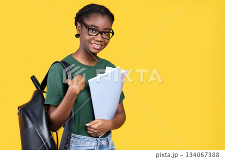 Cheerful African American Female Student Posing Holding Notebooks Smiling To Camera Standing In Studio Over Yellow Background. Students Lifestyle, University And College Education Concept 134067388