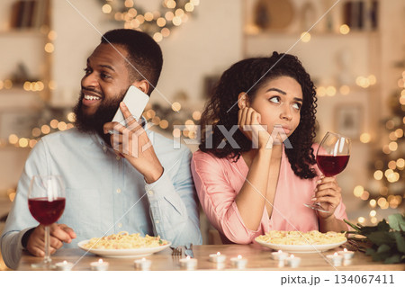 Bad Date. Unhappy Sad African American Woman Is Getting Bored Sitting On Date In Restaurant While Her Smiling Boyfriend Talking On Mobile Phone, Ignoring His Girlfriend. Relationship Problem Bad Date. Unhappy Sad African American Woman Is Getting Bored Sitting On Date In Restaurant While Her Smiling Boyfriend Talking On Mobile Phone, Ignoring His Girlfriend. Relationship Problem 134067411