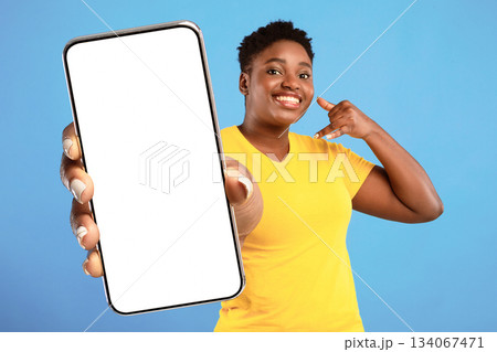 Call Me. Positive Plus Size African Woman Holding Hand Near Ear Like Phone And Pointing Finger At Camera Recommending To Contact Her Standing Over Blue Background. Studio Shot Call Me. Positive Plus Size African Woman Holding Hand Near Ear Like Phone And Pointing Finger At Camera Recommending To Contact Her Standing Over Blue Background. Studio Shot 134067471