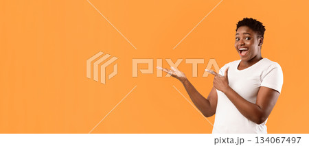 Excited Plus-Size Black Woman Showing Invisible Object Pointing Fingers Aside Advertising Your Text Posing Standing On Yellow Studio Background, Smiling To Camera. Blank Space, Panorama Excited Plus-Size Black Woman Showing Invisible Object Pointing Fingers Aside Advertising Your Text Posing Standing On Yellow Studio Background, Smiling To Camera. Blank Space, Panorama 134067497