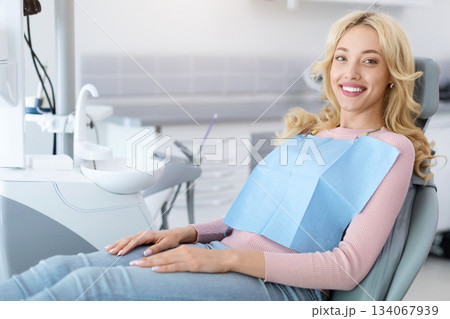 Side view of pretty blonde young woman patient sitting in dental chair and smiling, copy space. Cheerful millennial lady showing beautiful white smile after treatment at modern dental clinic 134067939