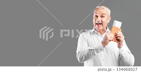 Vacation Time. Overjoyed mature man showing his passport and boarding pass isolated over gray studio wall 134068027