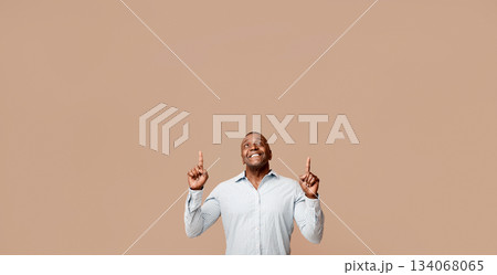 Look up there. Positive african middle aged man pointing up, looking at free space, orange studio background 134068065