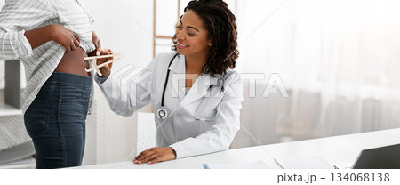 Smiling african woman dietologist checking female patient body fat index with caliper, clinic interior, close up Smiling african woman dietologist checking female patient body fat index with caliper, clinic interior, close up 134068138