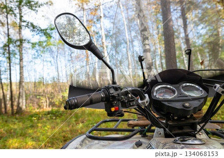 left brake handle of an ATV, windshield, and rear view mirrors. Quad bike or ATV stands in forest. All Terrain Vehicle 134068153