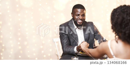 Happy black guy courting his woman, having date in fancy restaurant, man holding woman hand Happy black guy courting his woman, having date in fancy restaurant, man holding woman hand 134068166