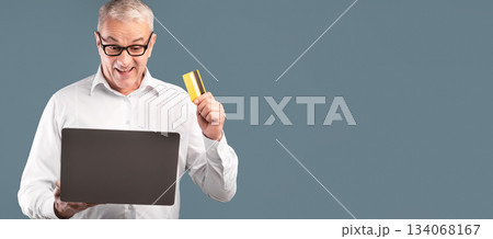 Easy Payment. Excited elderly man in glasses holding credit card and laptop for online shopping over blue studio wall 134068167