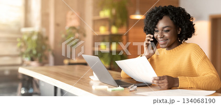 Young black smiling businesswoman talking to colleagues by phone, working with laptop at cafe 134068190