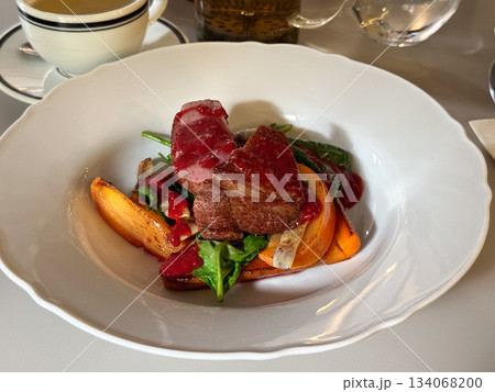 Meat with vegetables and berry sauce on a white plate. Culinary craftsmanship, contrast of colors, and fine dining mood through modern plating. 134068200