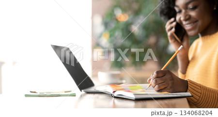 Close up of cheery black lady taking notes while having phone conversation at cafe, looking for job, free space Close up of cheery black lady taking notes while having phone conversation at cafe, looking for job, free space 134068204