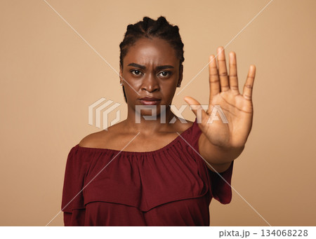 Young angry african american woman in casual outfit making the hand stop sign against beige studio background, closeup, copy space. Stop abuse, discrimination, violence concept 134068228