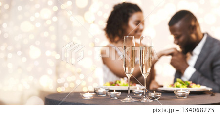 Black man and woman having romantic date at restaurant, eating meal and drinking champagne, selective focus on glasses of champagne 134068275