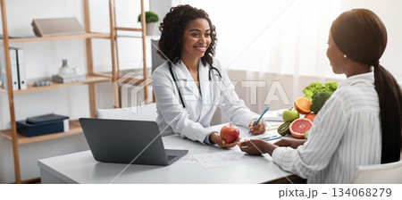 Happy nutritionist black woman giving consultation to patient with healthy fruit and vegetable, nutrition and diet concept 134068279