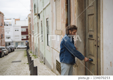 Man with denim jacket reenters residence along textured wall 134070253