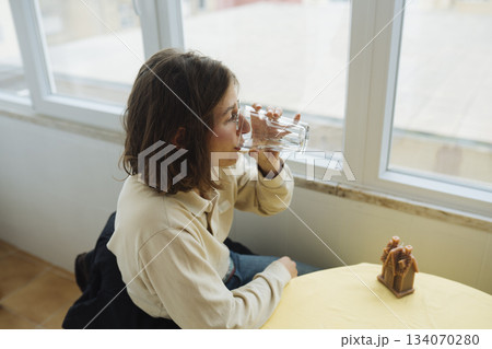 Tranquil woman pauses thoughtfully at window with soft illumination Tranquil woman pauses thoughtfully at window with soft illumination 134070280
