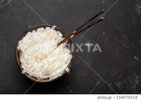 Rice cooked plain noodles with chopsticks dark bowl top view black rustic background copy space 134070318