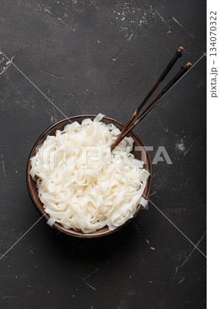 Rice cooked plain noodles with chopsticks dark bowl top view black rustic background 134070322