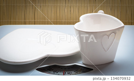 Empty plate saucer and mug cup on weighing scale. 134070932